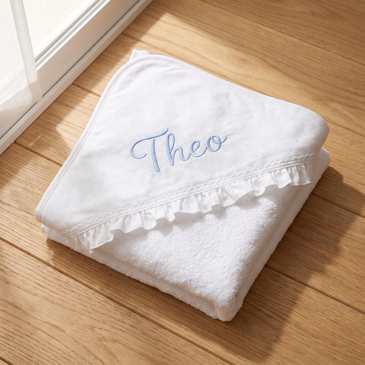 Personalisiertes Kapuzenhandtuch für Babys mit hellblau besticktem Namen und weißer Rüsche